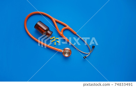Healthcare concept Yellow pills and stethoscope on blue background. Top view with copy space. Healthcare concept Yellow pills and stethoscope on blue background. Top view with copy space. 74833491