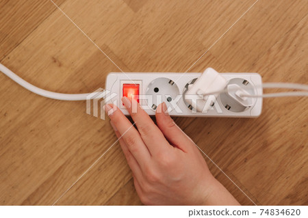 Top view of female hand turn on the extension cord at home. White cable connector Top view of female hand turn on the extension cord at home. White cable connector 74834620