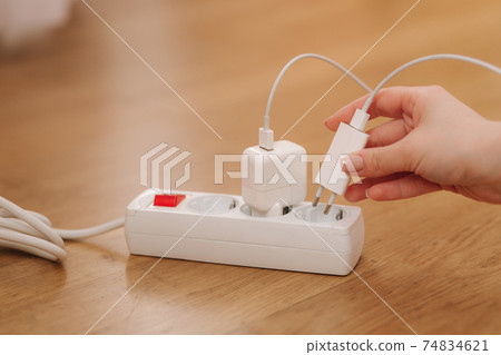 Woman pluging the wire into white extension cord. Close up of female hand put cabel Woman pluging the wire into white extension cord. Close up of female hand put cabel 74834621
