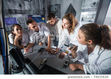 Five adults solving conundrums together in quest room in view as abandoned lab 74835630