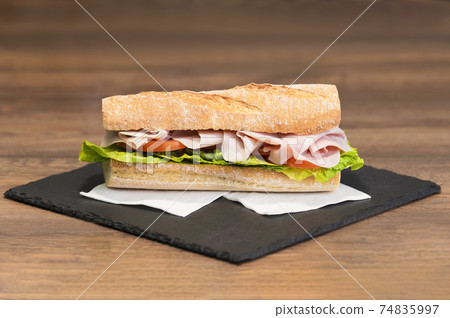 Select focus of a delicious looking meat and vegetables sub sandwich on a slate tray Select focus of a delicious looking meat and vegetables sub sandwich on a slate tray 74835997