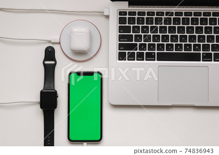 Charging of different devices on working place. Few cabel for wireless charging. Laptop, smart watch, smart phone with green screen and witeless headphones on white table. Top view. Mock up. Place for Charging of different devices on working place. Few cabel for wireless charging. Laptop, smart watch, smart phone with green screen and witeless headphones on white table. Top view. Mock up. Place for 74836943