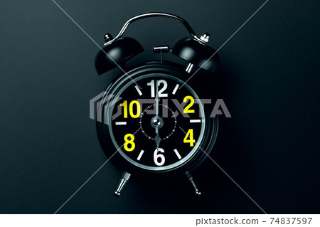 A stylish black alarm clock with yellow and white numbers stands on a dark background. Blank for the A stylish black alarm clock with yellow and white numbers stands on a dark background. Blank for the 74837597
