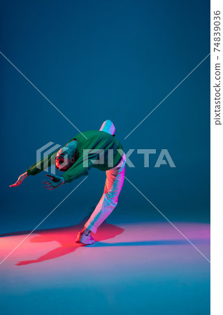 Stylish sportive boy dancing hip-hop in stylish clothes on colorful background at dance hall in neon light. Youth culture, movement, style and fashion, action. 74839036