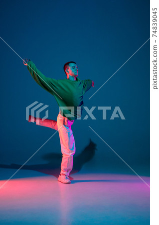 Stylish sportive boy dancing hip-hop in stylish clothes on colorful background at dance hall in neon light. Youth culture, movement, style and fashion, action. 74839045