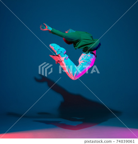 Stylish sportive boy dancing hip-hop in stylish clothes on colorful background at dance hall in neon light. Youth culture, movement, style and fashion, action. 74839061