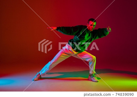 Stylish sportive boy dancing hip-hop in stylish clothes on colorful background at dance hall in neon light. Youth culture, movement, style and fashion, action. 74839090
