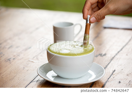 Hot matcha latte or green tea in white ceramic cup with saucer stired Hot matcha latte or green tea in white ceramic cup with saucer stired 74842647