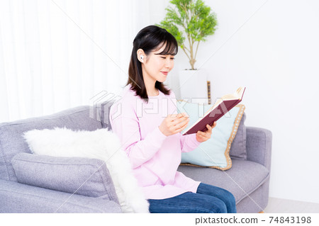 一個年輕的女人，一邊聽音樂在沙發上看 74843198