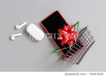 Smartphone, white wireless earphones and bow flying from the toy shopping cart Smartphone, white wireless earphones and bow flying from the toy shopping cart 74843583