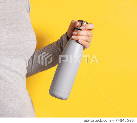 Woman in grey tee holding grey insulated bottle on yellow background Woman in grey tee holding grey insulated bottle on yellow background 74843586