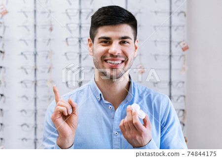 Happy guy holding contact eye lenses in optics shop Happy guy holding contact eye lenses in optics shop 74844175