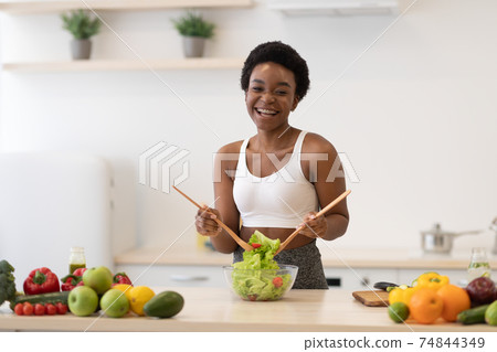 African Lady Cooking Salad Slimming Standing Wearing Fitwear In Kitchen African Lady Cooking Salad Slimming Standing Wearing Fitwear In Kitchen 74844349