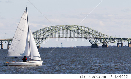 Small sailboat sailing past the great south bay bridge Small sailboat sailing past the great south bay bridge 74844922