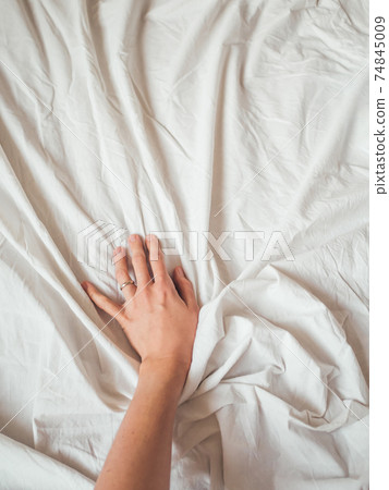 Woman's hand on background of crumpled bed sheet. Creased white linen. Woman touches unmade bed. Cozy imperfect house. Non-ideal cozy home. Woman's hand on background of crumpled bed sheet. Creased white linen. Woman touches unmade bed. Cozy imperfect house. Non-ideal cozy home. 74845009