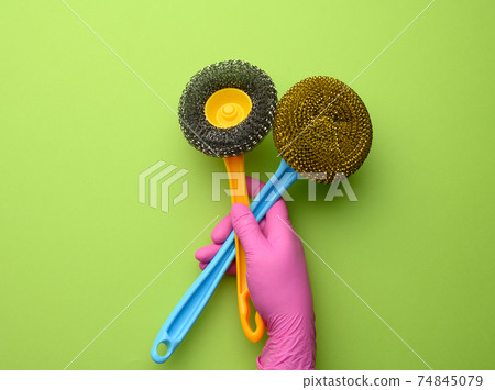 female hand in purple rubber gloves holds a plastic cleaning brush on green background 74845079