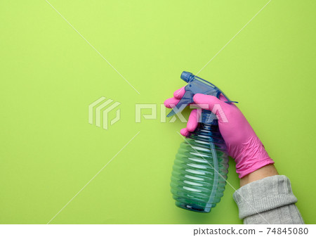 female hand in pink glove holds a transparent plastic spray bottle on green background 74845080