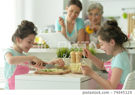 Cute girls preparing delicious fresh salad in kitchen, mother and grandmother Cute girls preparing delicious fresh salad in kitchen, mother and grandmother 74845129