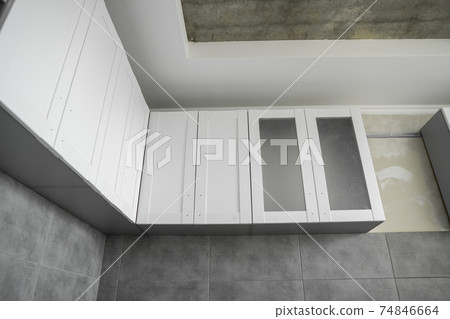 Custom kitchen cabinets installation with a white furniture facades mdf. Gray modular kitchen from chipboard material on a various stages of installation. A frame furniture fronts mdf profile. 74846664