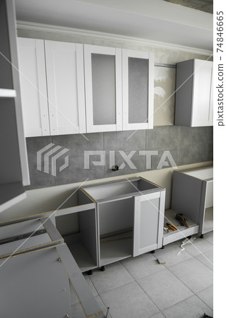 Custom kitchen cabinets installation with a furniture facades mdf. Gray modular kitchen from chipboard material on a various stages of installation. A frame furniture fronts mdf profile. 74846665