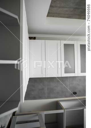 Custom kitchen cabinets installation with a furniture facades mdf. Gray modular kitchen from chipboard material on a various stages of installation. A frame furniture fronts mdf profile. 74846666