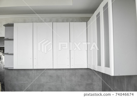 Custom kitchen cabinets installation with a white furniture facades mdf. Gray modular kitchen from chipboard material on a various stages of installation. A frame furniture fronts mdf profile. 74846674