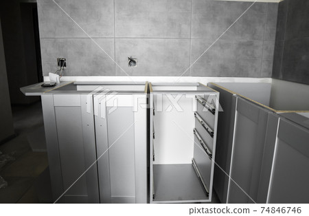 Lower custom kitchen cabinets installation with a furniture facades mdf. Gray modular kitchen from chipboard material on a various stages of installation. A frame furniture fronts mdf profile. 74846746