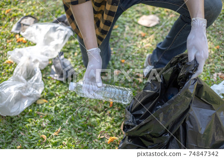 Male volunteers carry water bottles or plastic bags that have fallen in the park put them in trash cans, Environmental protection or volunteering for charity, Waste disposal through recycling. Male volunteers carry water bottles or plastic bags that have fallen in the park put them in trash cans, Environmental protection or volunteering for charity, Waste disposal through recycling. 74847342