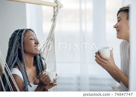 Two girls having coffee in a light room and looking relaxed 74847747