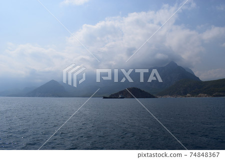 Cargo ship sailing by the coast against cloudy blue sky and rippled sea near the Turtle Island Cargo ship sailing by the coast against cloudy blue sky and rippled sea near the Turtle Island 74848367