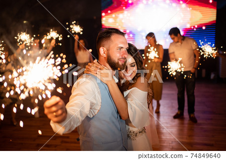 newlyweds with sparklers in night say goodbye to guests in the restaurant newlyweds with sparklers in night say goodbye to guests in the restaurant 74849640