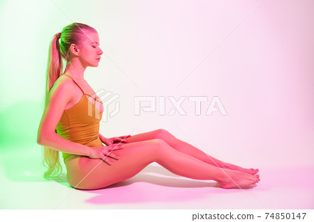 Tired female gymnast sitting on floor in studio Tired female gymnast sitting on floor in studio 74850147