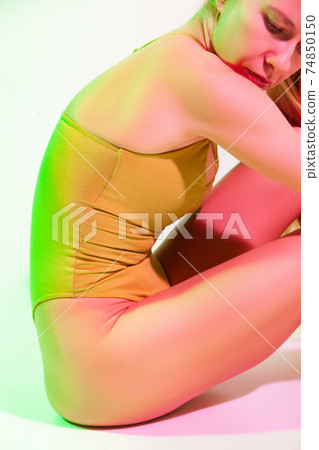 Tired female gymnast sitting on floor in studio 74850150