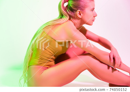 Tired female gymnast sitting on floor in studio Tired female gymnast sitting on floor in studio 74850152