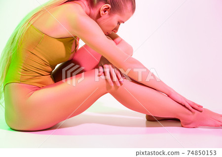 Tired female gymnast sitting on floor in studio Tired female gymnast sitting on floor in studio 74850153