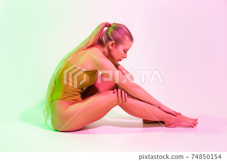 Tired female gymnast sitting on floor in studio Tired female gymnast sitting on floor in studio 74850154