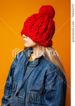 Hipster woman in red knitted hat against orange background Hipster woman in red knitted hat against orange background 74850207