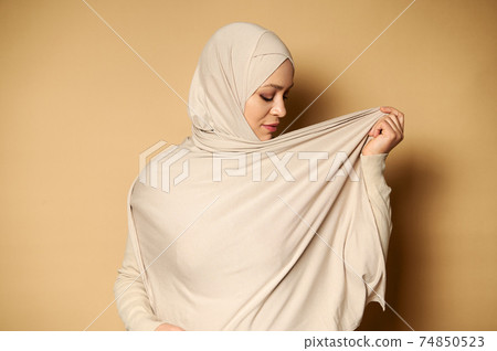 Side portrait of an elegant muslim woman wearing hijab. Strict formal outfit and elegant appearance. Islamic fashion. Beige background with copy space. Side portrait of an elegant muslim woman wearing hijab. Strict formal outfit and elegant appearance. Islamic fashion. Beige background with copy space. 74850523