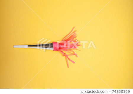 Party horn and scattered shiny confetti on orange background 74850569