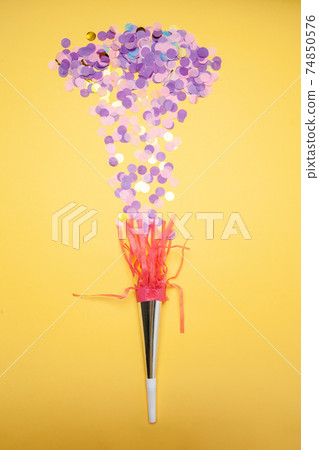 Heap of purple confetti and party horn arranged on yellow background 74850576