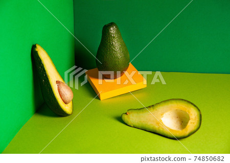 Whole ripe avocado on yellow board near halved fruit in green box 74850682