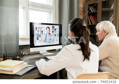 Sick senior man and young general practitioner sitting in front of computer Sick senior man and young general practitioner sitting in front of computer 74851419