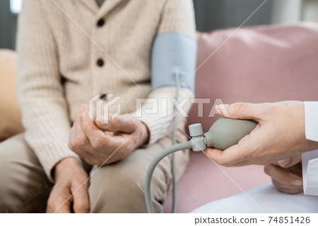 Hand of young doctor pressing pump of tonometer while measuring blood pressure 74851426
