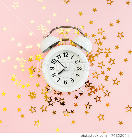 Alarm clock covered golden stars confetti, decoration on a pink, festive background. Christmas or New Year pattern. Colorful celebration, birthday. 74852044