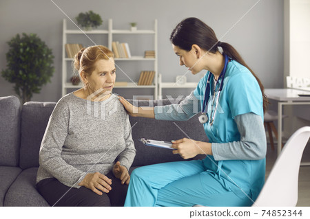 Worried mature woman talking to nurse or doctor who's comforting and supporting her 74852344