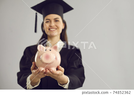 Pink piggy bank in the hands of a joyful female student standing on a gray background. 74852362