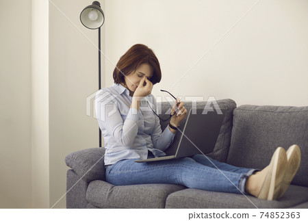Woman tired of working on laptop takes off glasses, rubs eyes and massages nose bridge Woman tired of working on laptop takes off glasses, rubs eyes and massages nose bridge 74852363