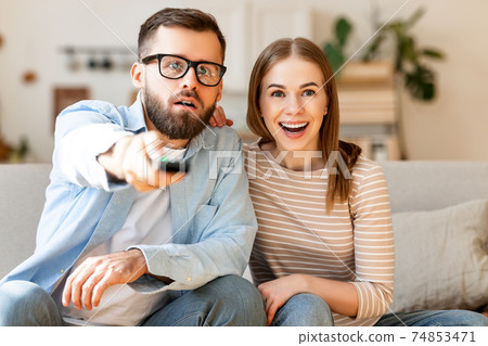 Amazed couple watching TV together Amazed couple watching TV together 74853471