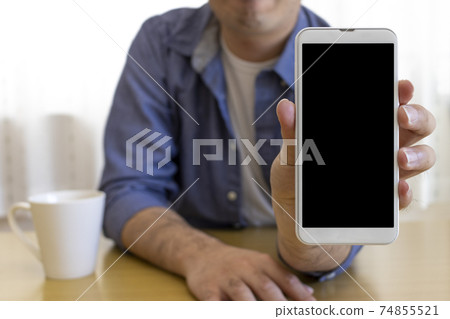 A man sitting on a chair and showing the screen of a smartphone (30s, Japanese, plain clothes) A man sitting on a chair and showing the screen of a smartphone (30s, Japanese, plain clothes) 74855521