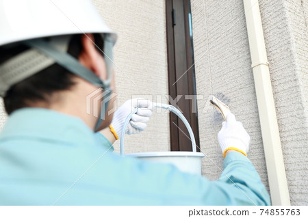 Male worker painting the exterior walls of a house Male worker painting the exterior walls of a house 74855763
